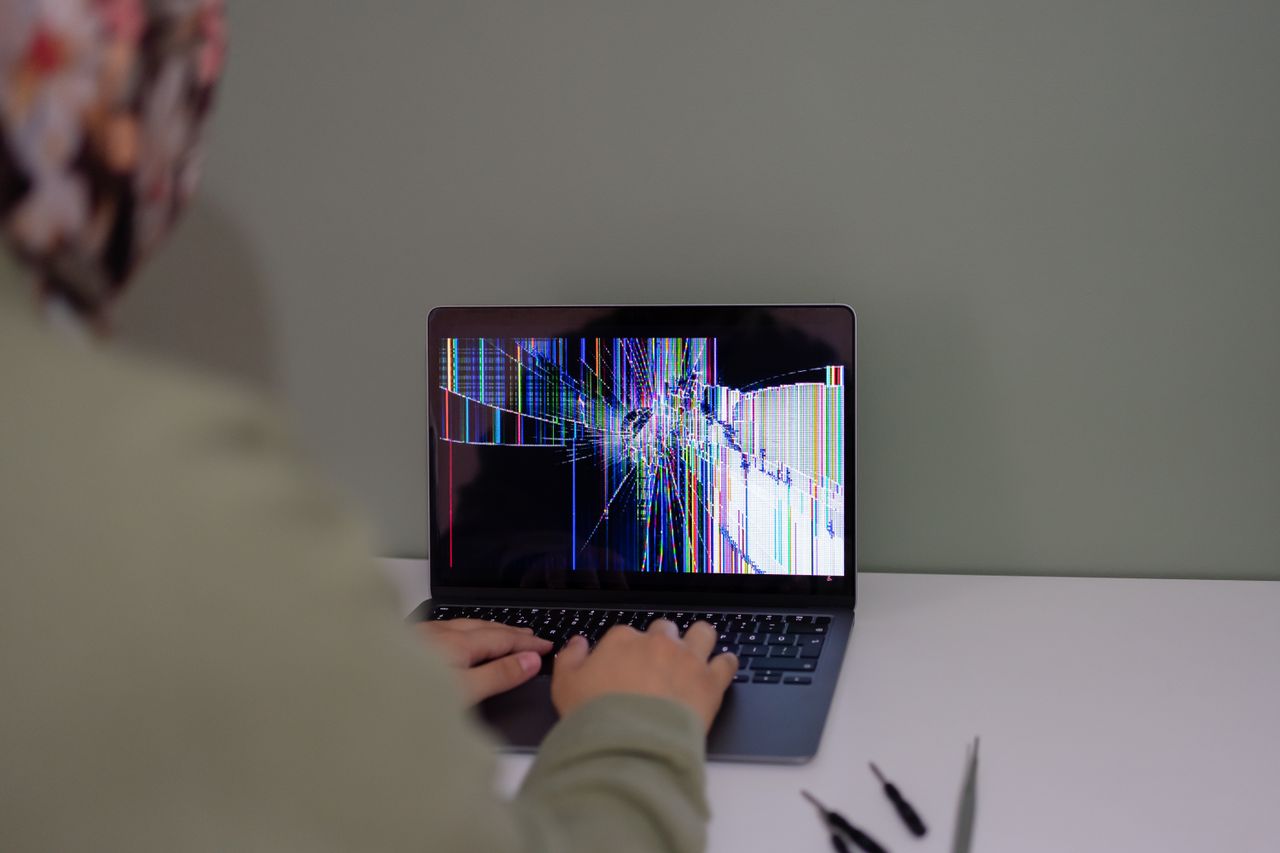 Home Adult working on a laptop with a cracked screen, indoors setting.